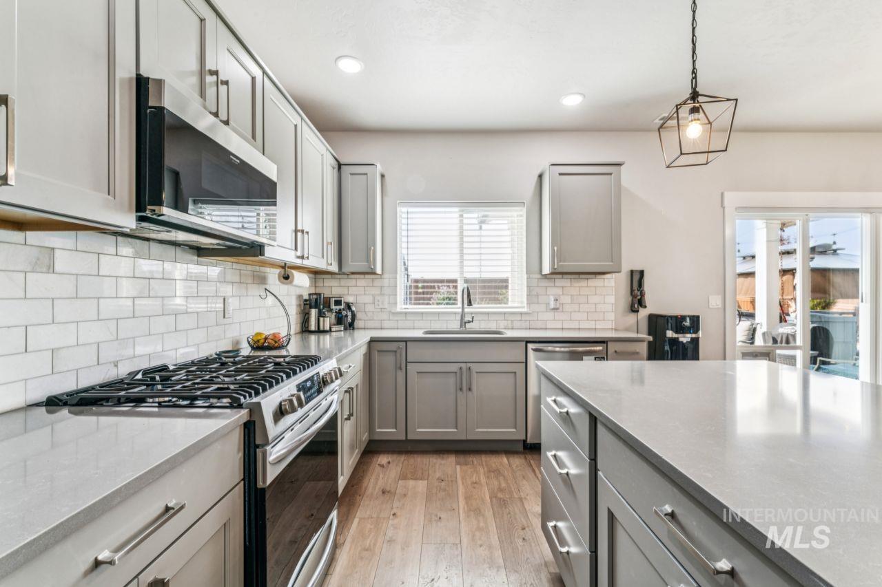 Kitchen with gray cabinetry, appliances with stainless steel finishes, decorative light fixtures, light stone countertops, and recessed lighting