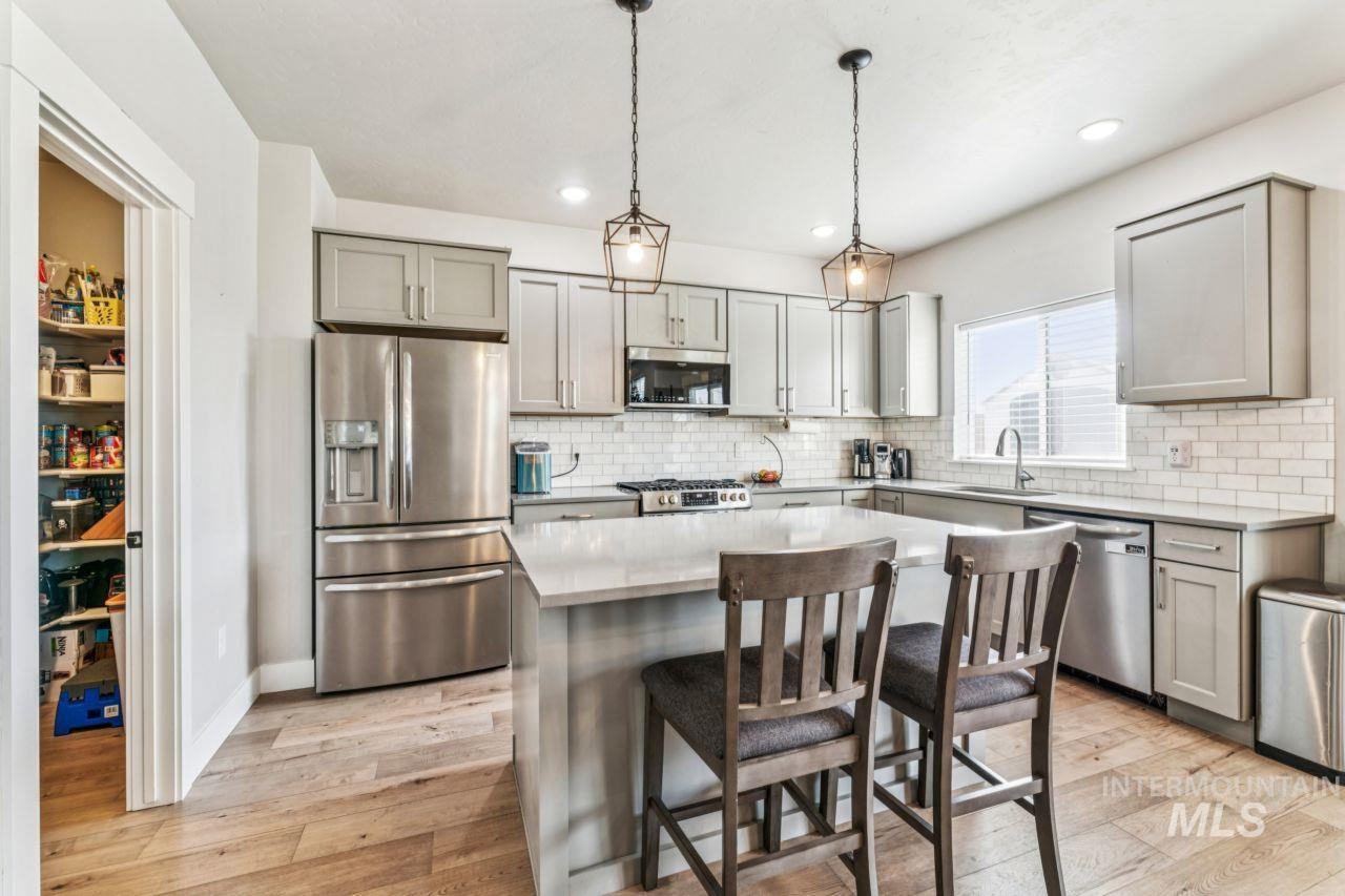Kitchen with appliances with stainless steel finishes, pendant lighting, gray cabinets, a center island, and light wood-style floors