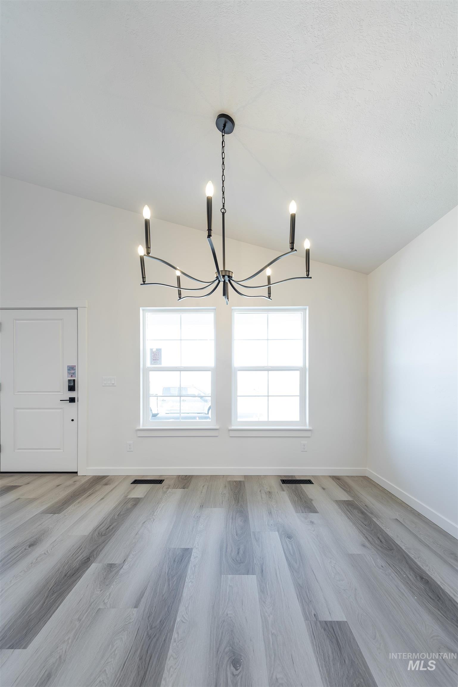 Unfurnished dining area featuring healthy amount of natural light, light wood-style flooring, vaulted ceiling, and a chandelier