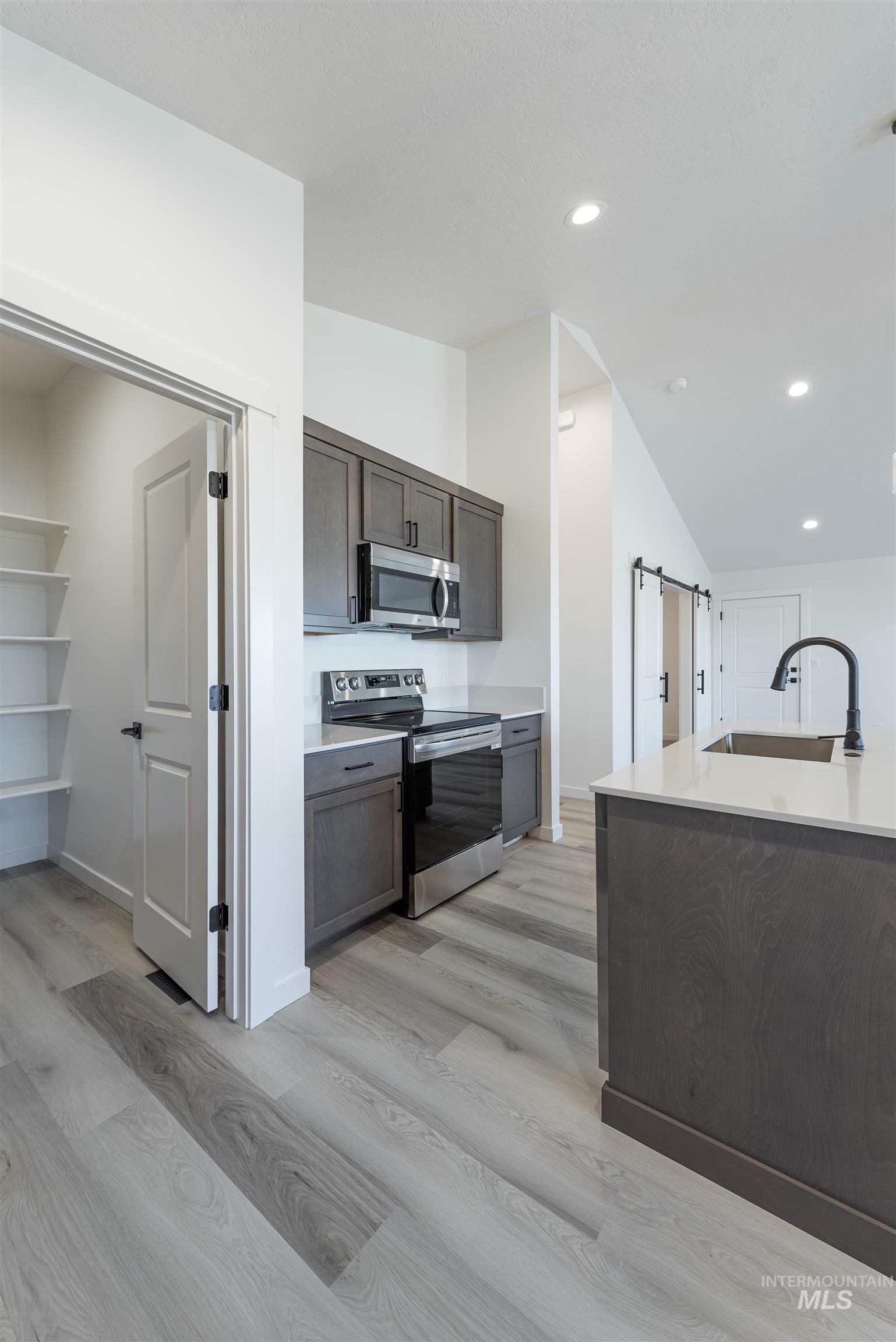Kitchen with appliances with stainless steel finishes, dark brown cabinets, recessed lighting, a barn door, and vaulted ceiling