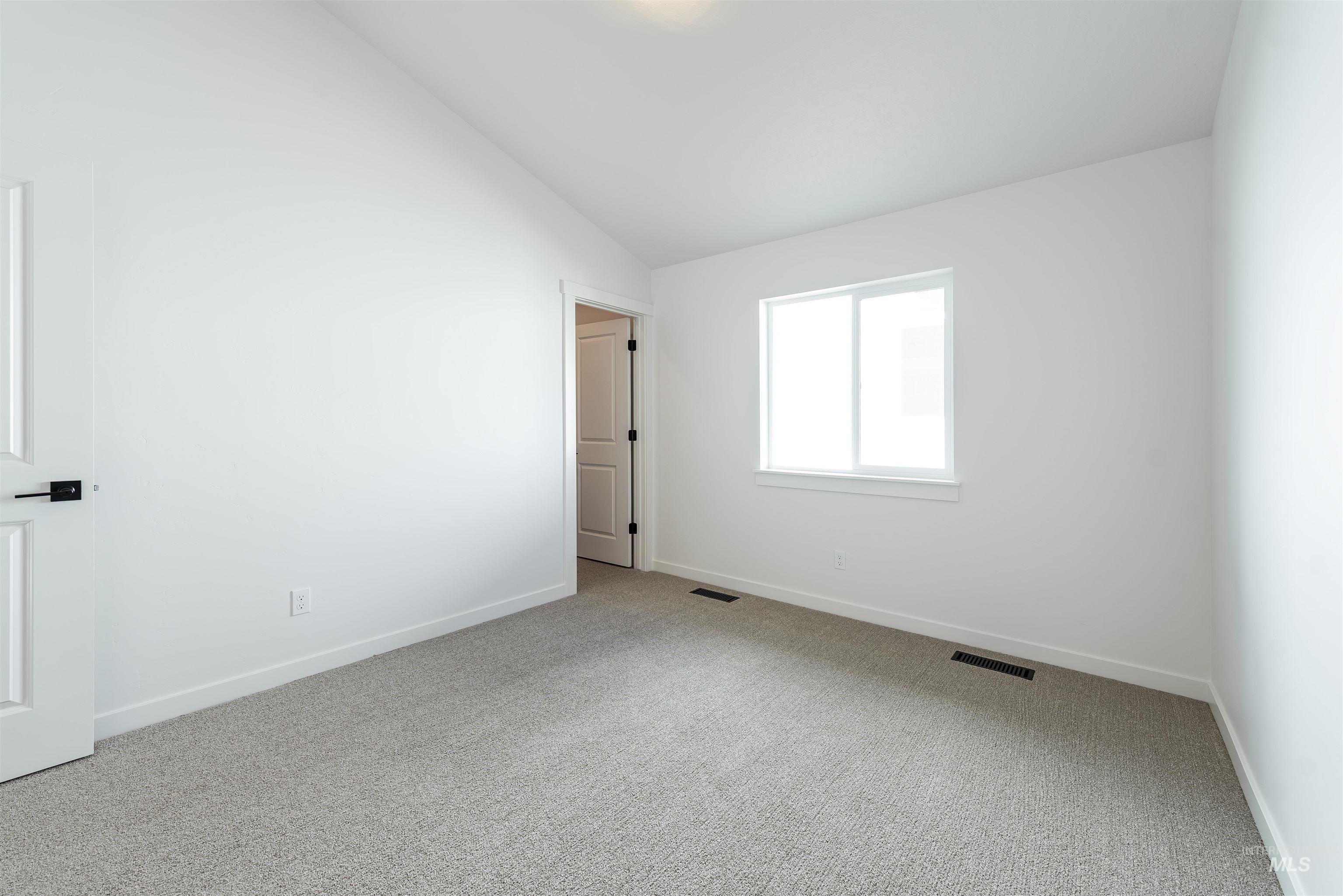 Carpeted empty room with vaulted ceiling and baseboards