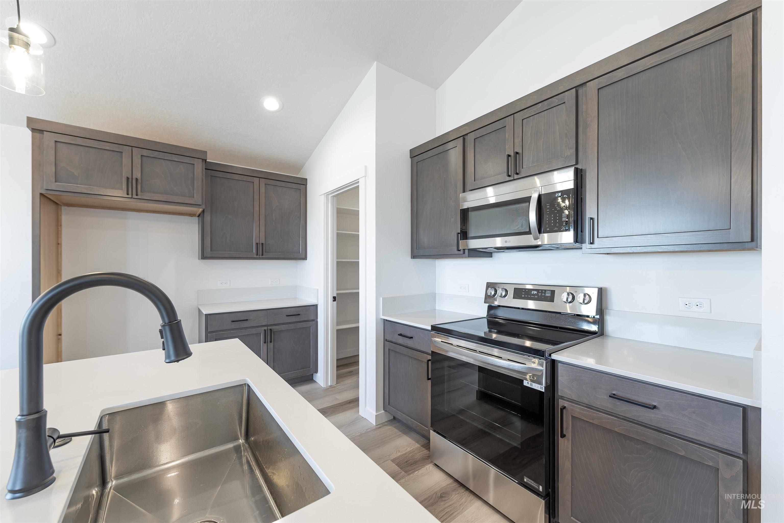 Kitchen with stainless steel appliances, light wood-style flooring, lofted ceiling, dark brown cabinets, and recessed lighting