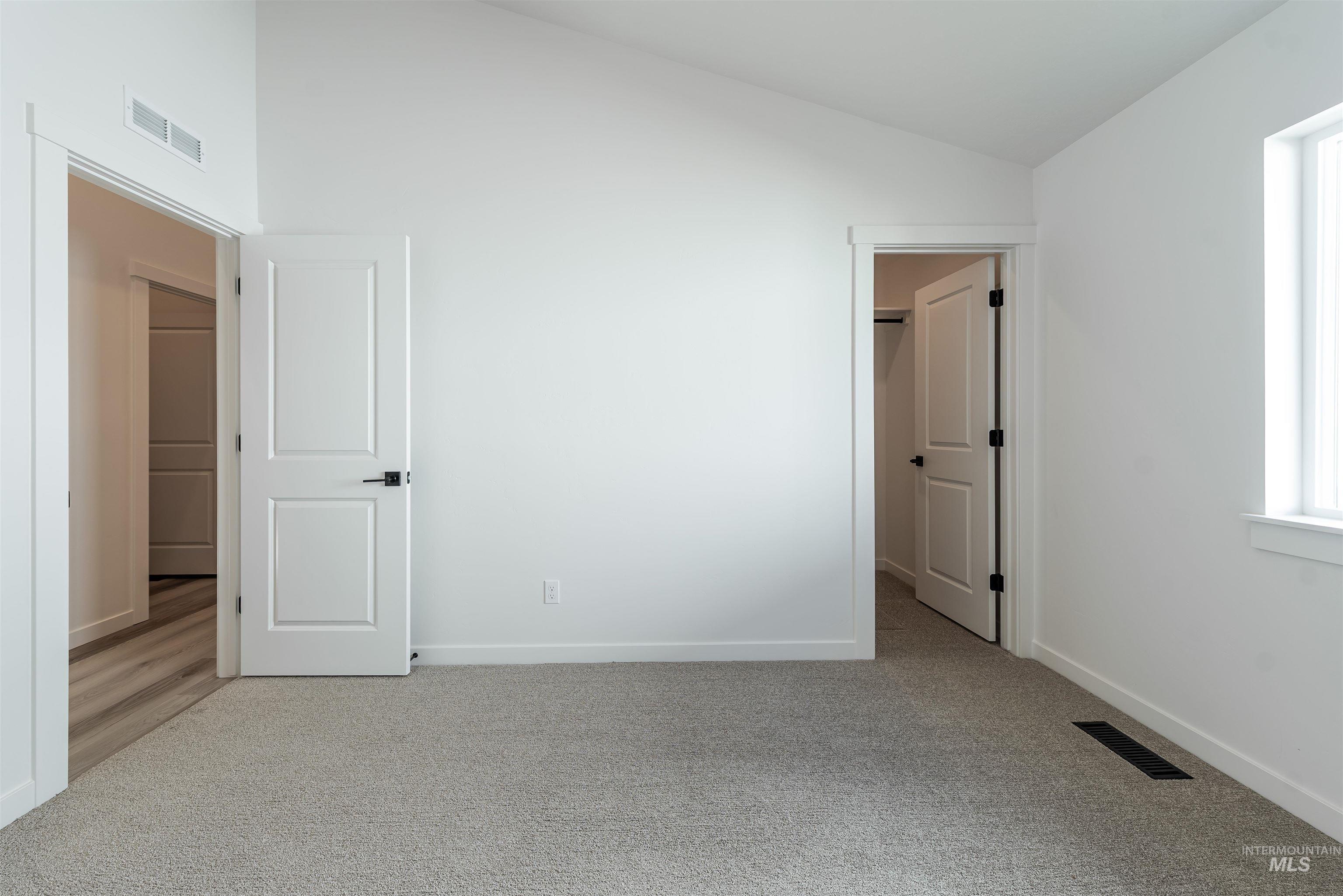 Unfurnished bedroom featuring light carpet and high vaulted ceiling