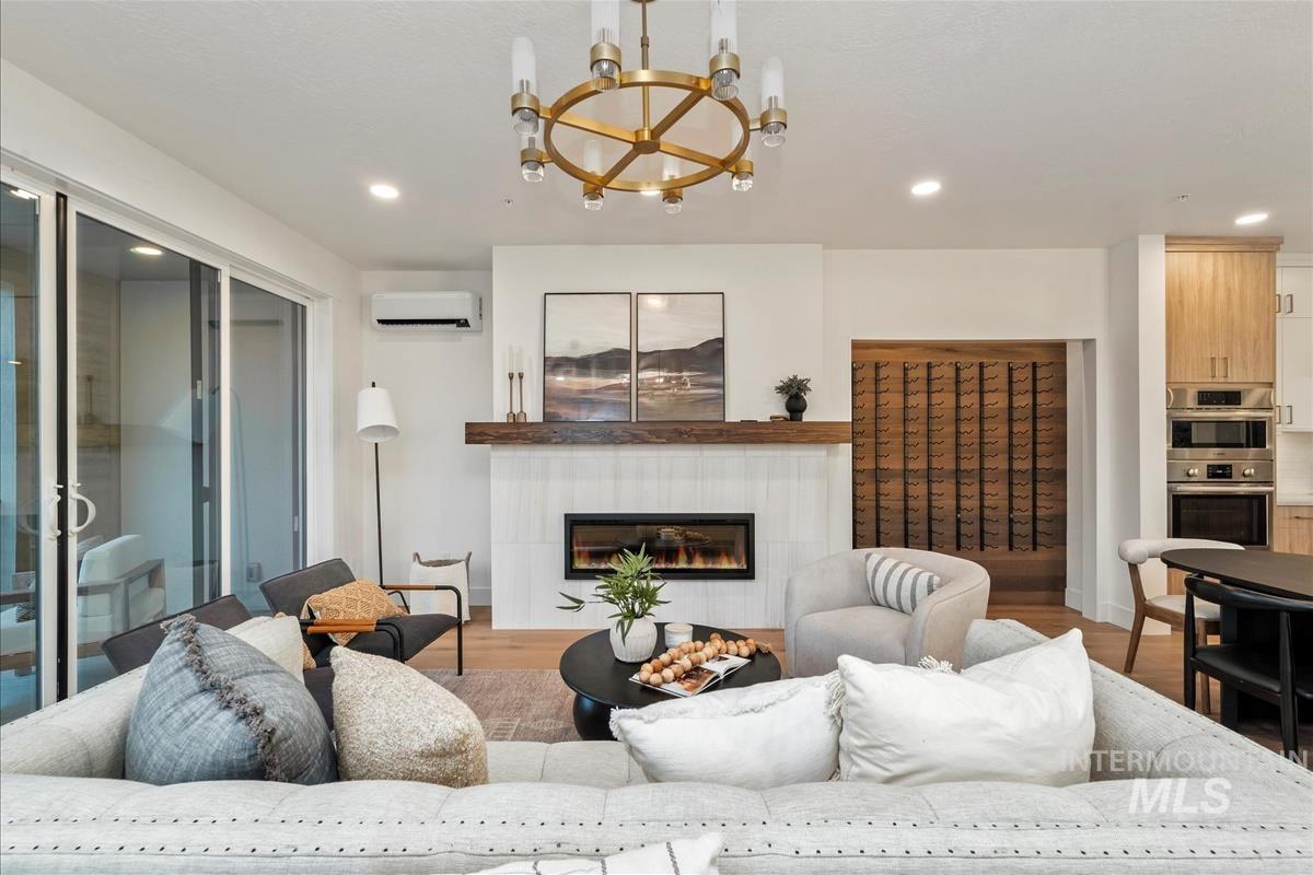Living area with a tile fireplace, light wood finished floors, recessed lighting, a wall unit AC, and a chandelier