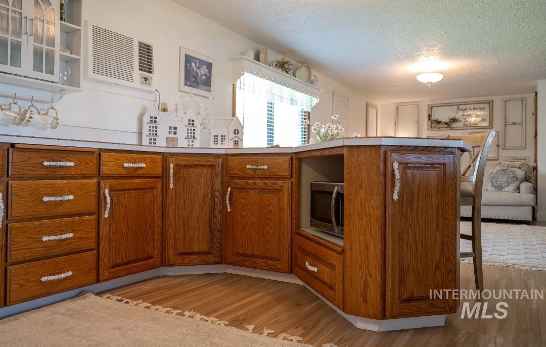 Kitchen featuring brown cabinetry, stainless steel microwave, a textured ceiling, light countertops, and light wood-style floors
