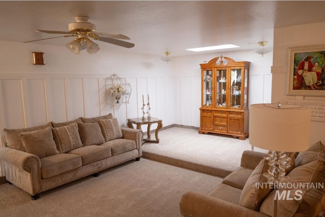 Carpeted living area featuring ceiling fan and a decorative wall