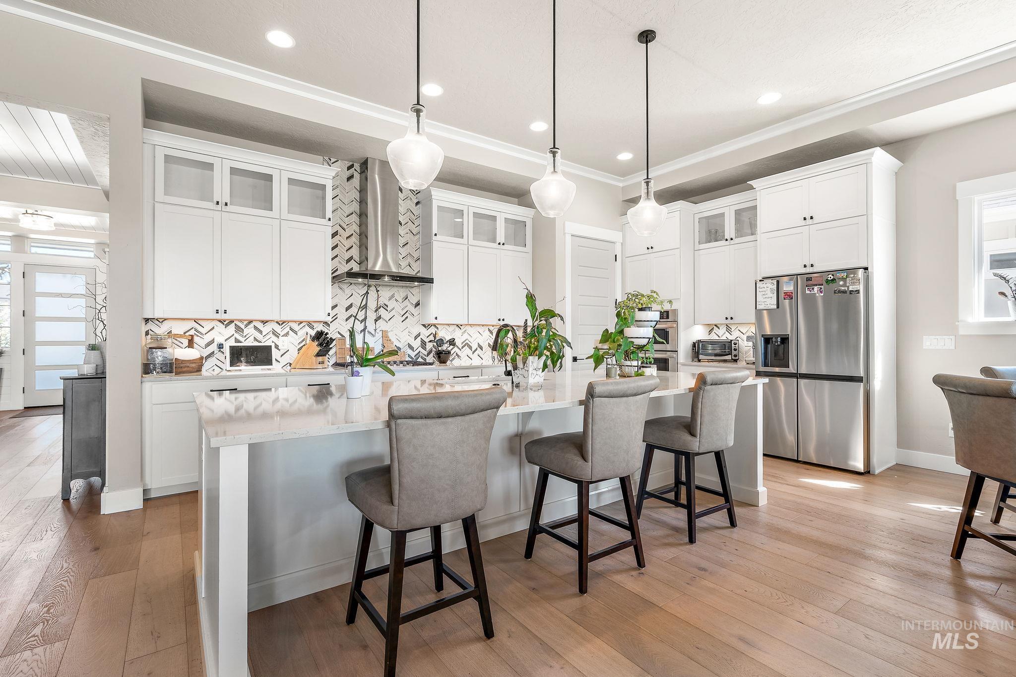 Kitchen with glass insert cabinets, backsplash, stainless steel fridge, a kitchen breakfast bar, and a center island with sink