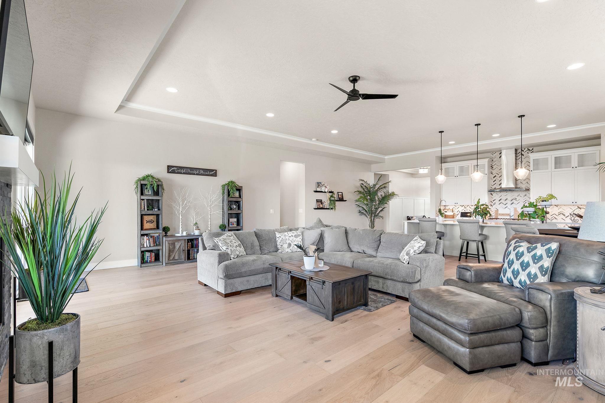 Living area featuring light wood-type flooring, ceiling fan, recessed lighting, and a tray ceiling