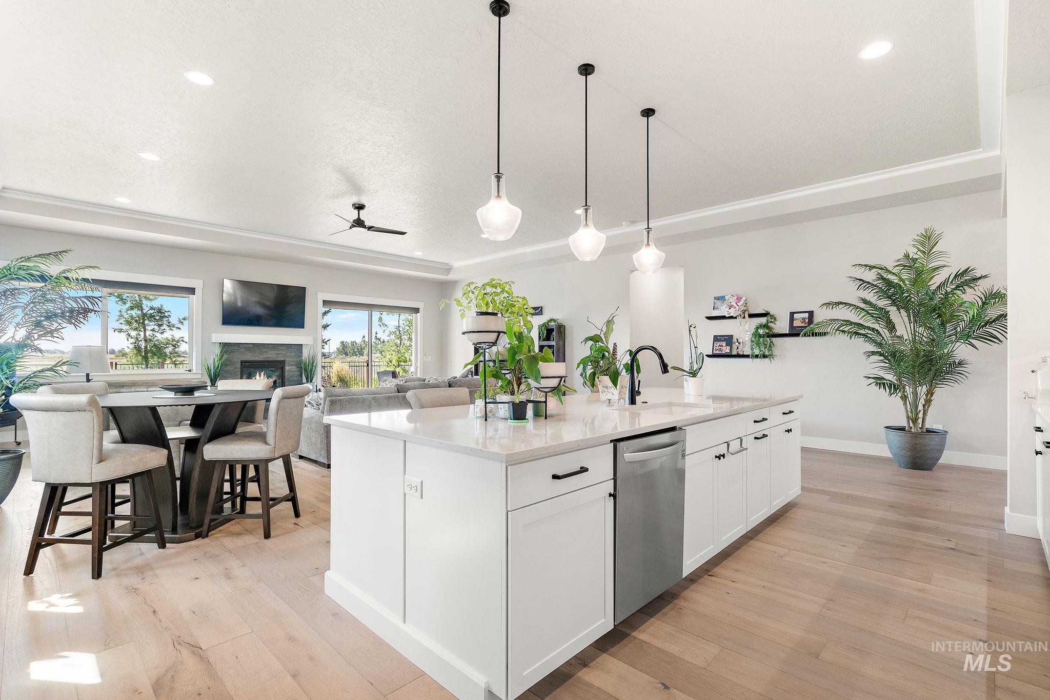 Kitchen featuring white cabinetry, a raised ceiling, ceiling fan, light wood-style flooring, and pendant lighting