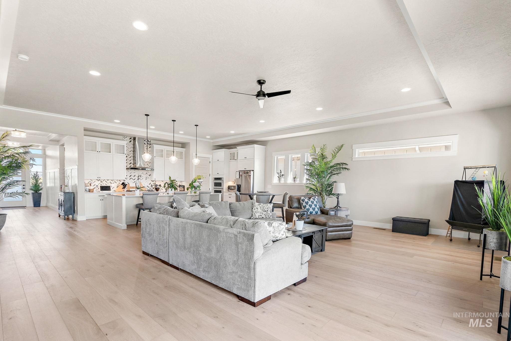 Living room with light wood-style floors, recessed lighting, a ceiling fan, and a tray ceiling