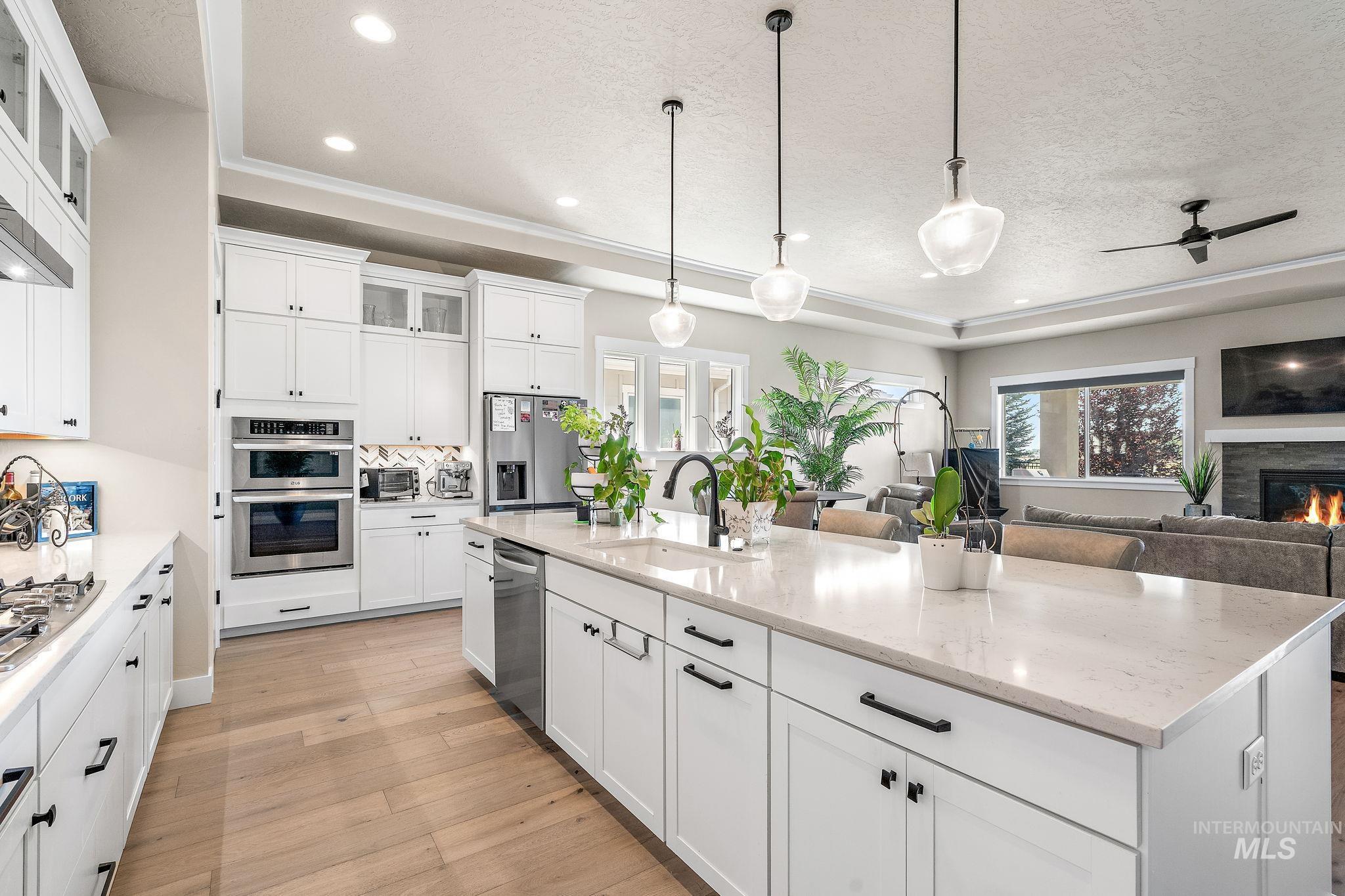Kitchen with glass insert cabinets, white cabinets, hanging light fixtures, light wood-type flooring, and appliances with stainless steel finishes