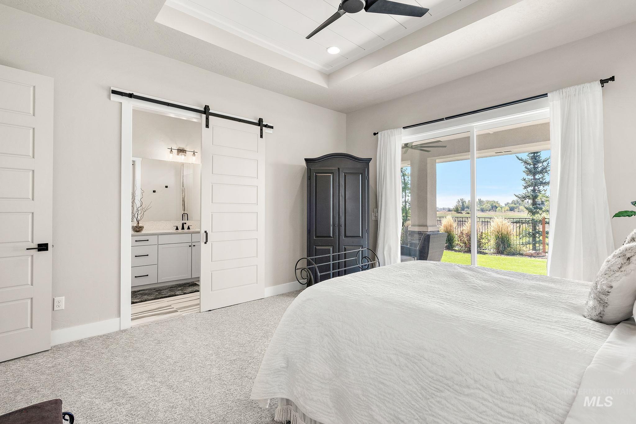 Bedroom featuring a tray ceiling, light carpet, recessed lighting, a barn door, and a ceiling fan