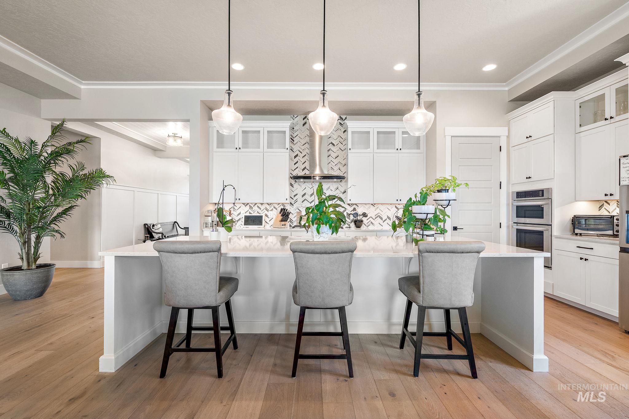 Kitchen featuring backsplash, a large island with sink, a kitchen bar, glass insert cabinets, and ornamental molding