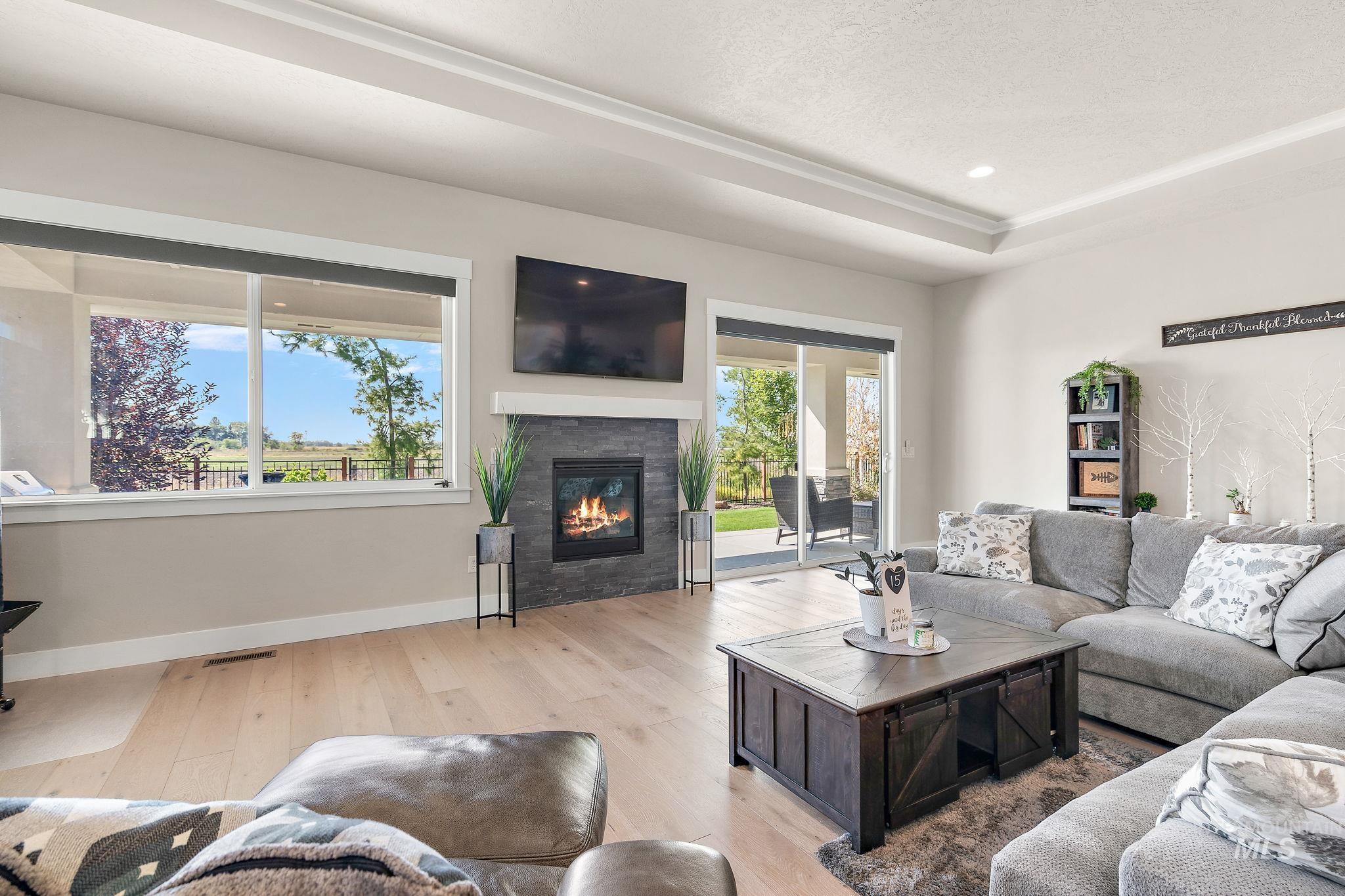 Living room featuring wood finished floors, a glass covered fireplace, a raised ceiling, and recessed lighting