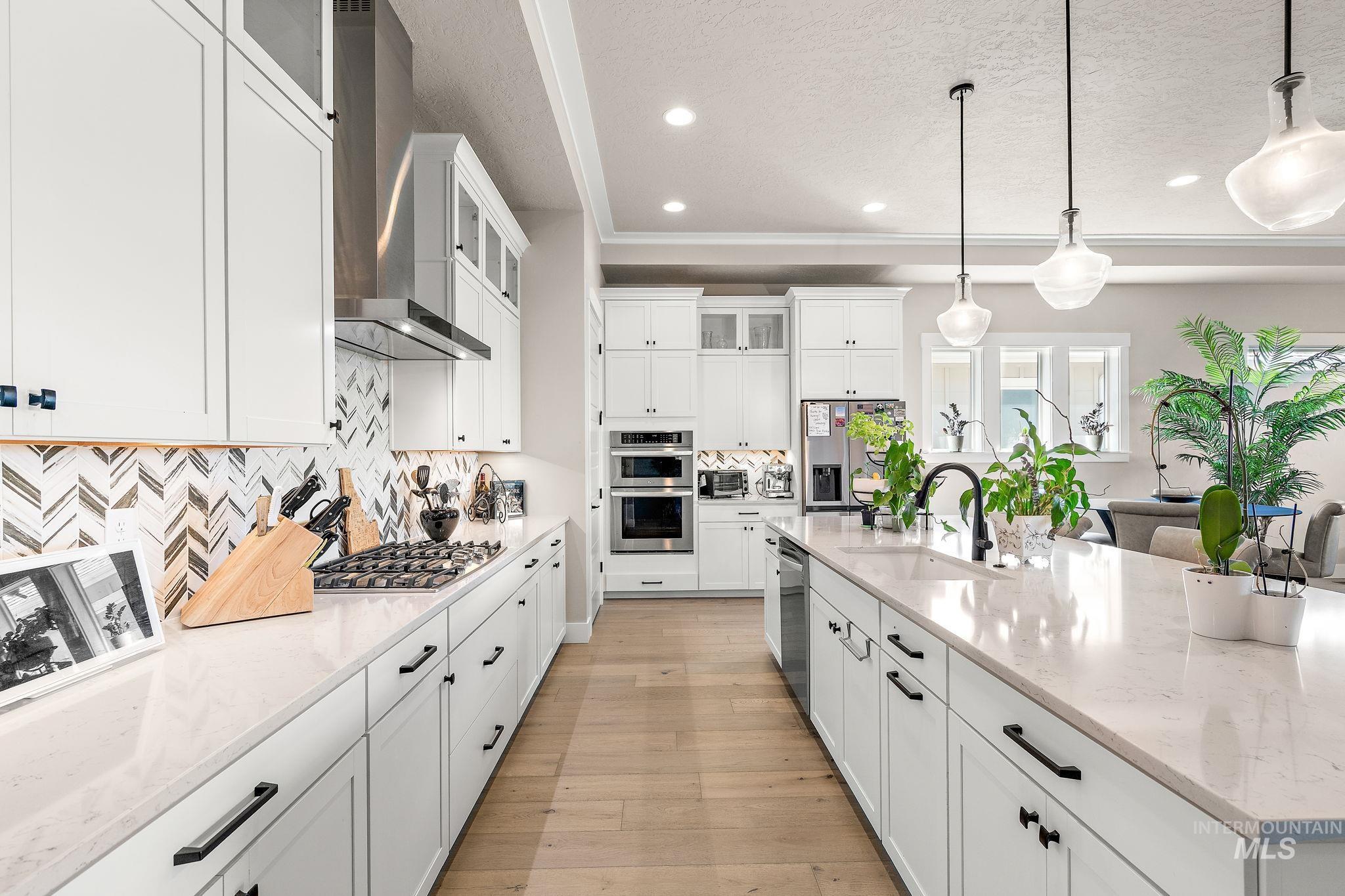 Kitchen featuring glass insert cabinets, white cabinetry, light stone countertops, pendant lighting, and wall chimney exhaust hood