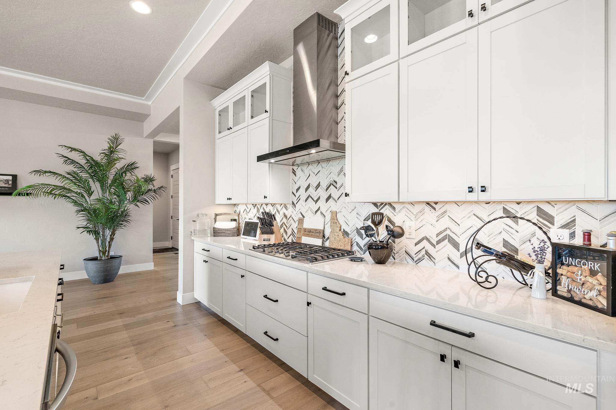 Kitchen featuring wall chimney range hood, white cabinetry, glass insert cabinets, light stone counters, and recessed lighting
