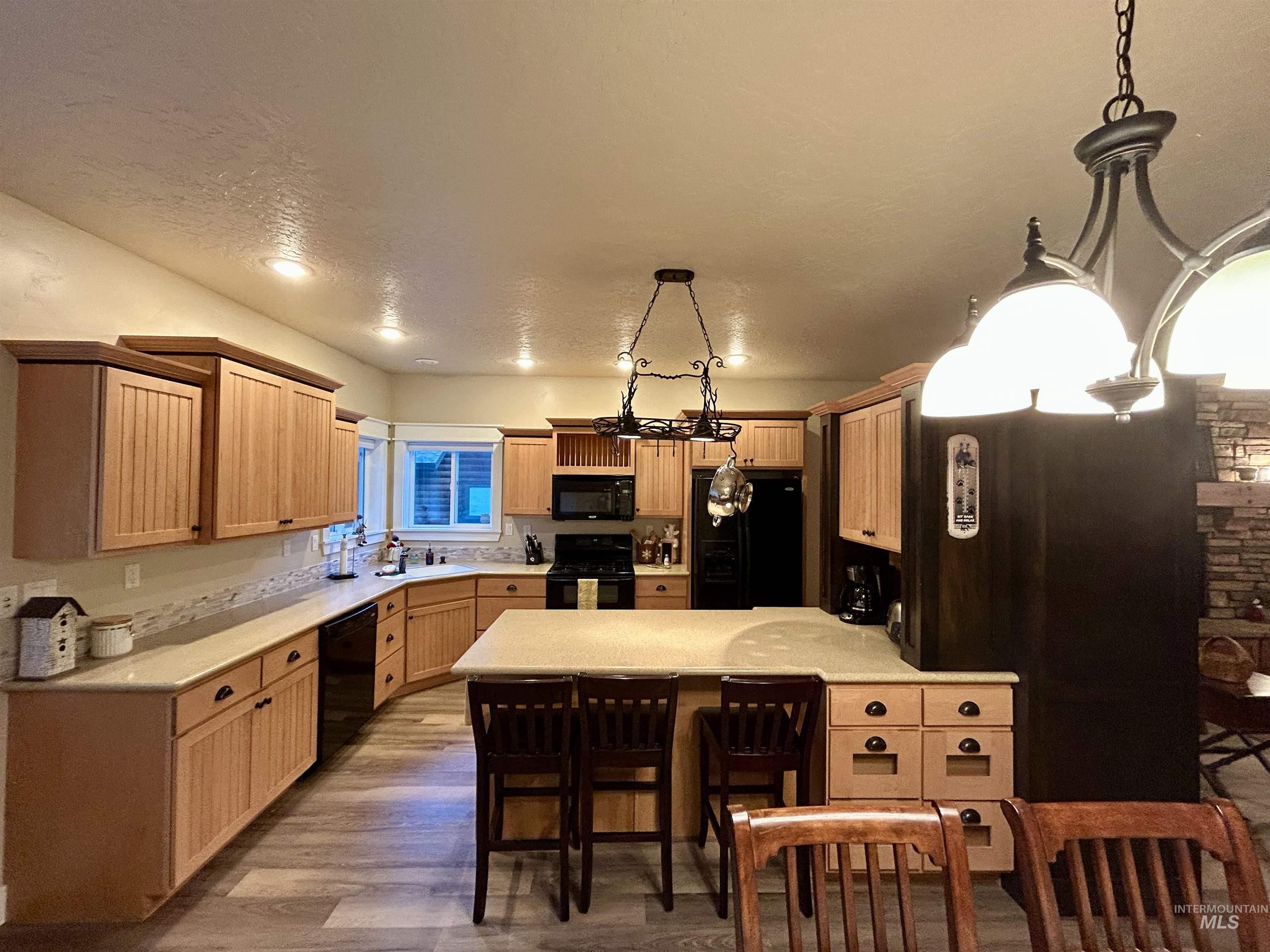 Kitchen featuring black appliances, light countertops, wood finished floors, a peninsula, and a kitchen breakfast bar