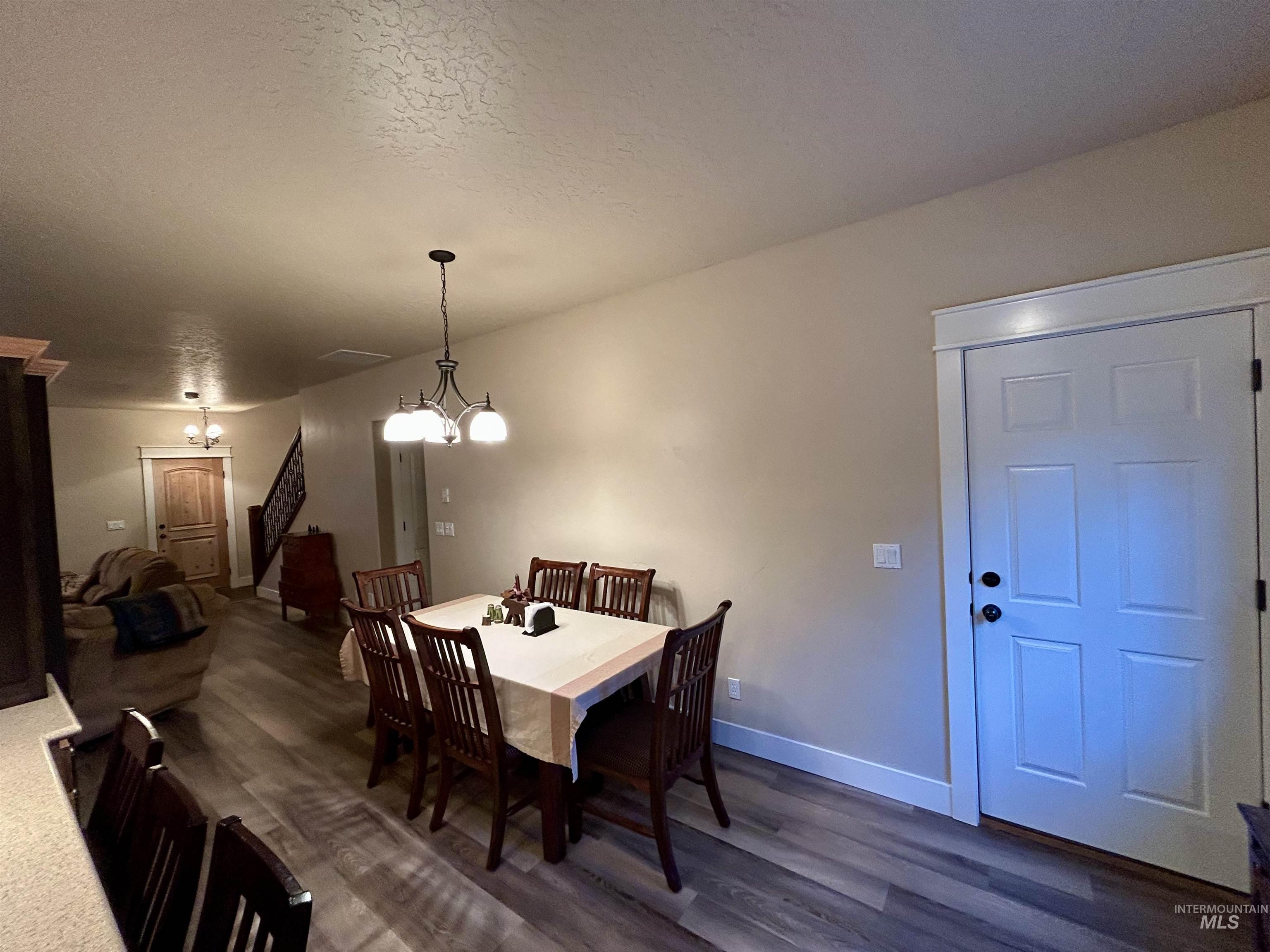 Dining area with dark wood-style flooring, a chandelier, stairs, and a textured ceiling