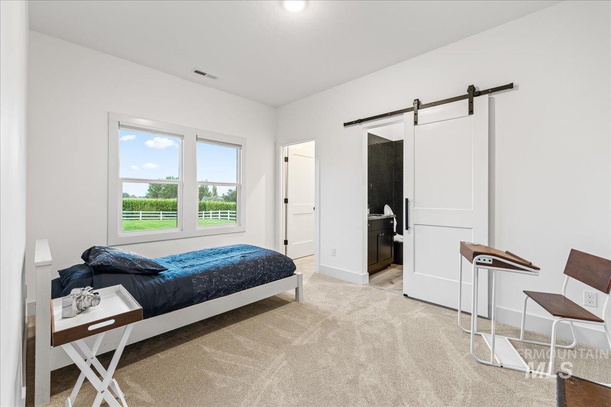 Bedroom featuring a barn door, light colored carpet, and connected bathroom