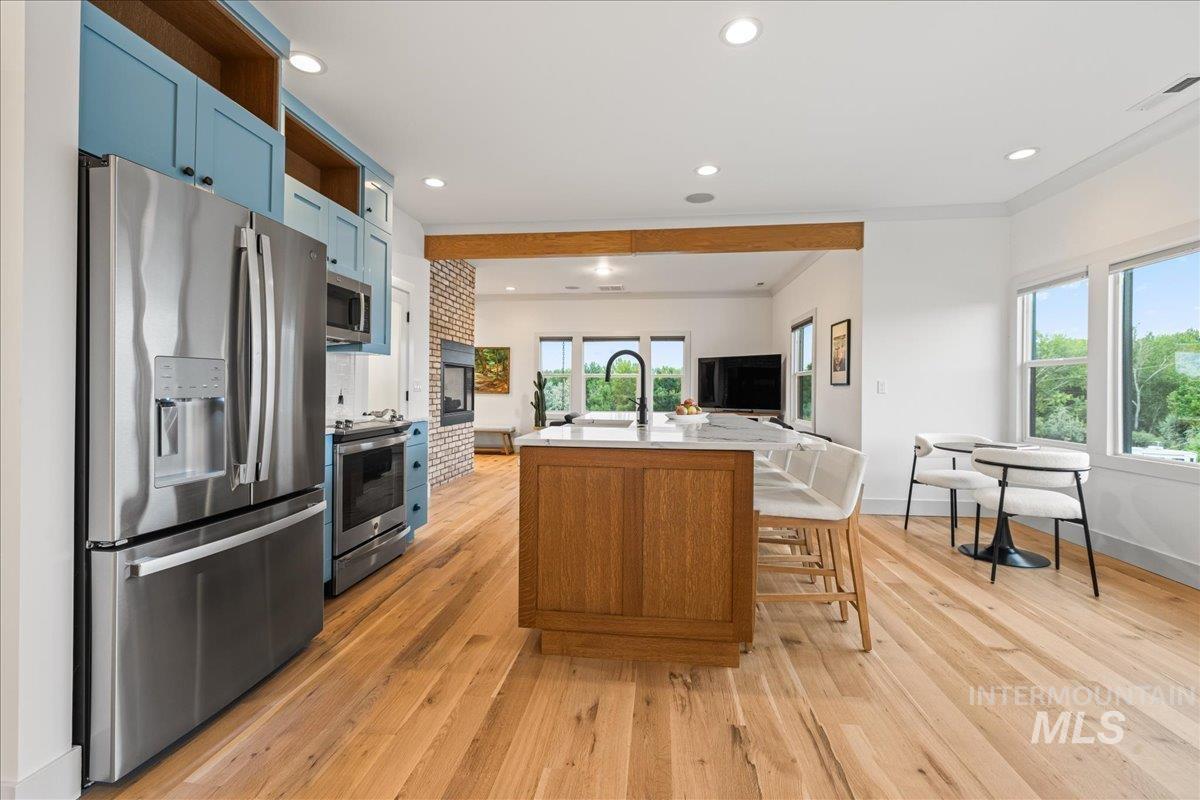 Kitchen featuring appliances with stainless steel finishes, blue cabinetry, an island with sink, recessed lighting, and open shelves
