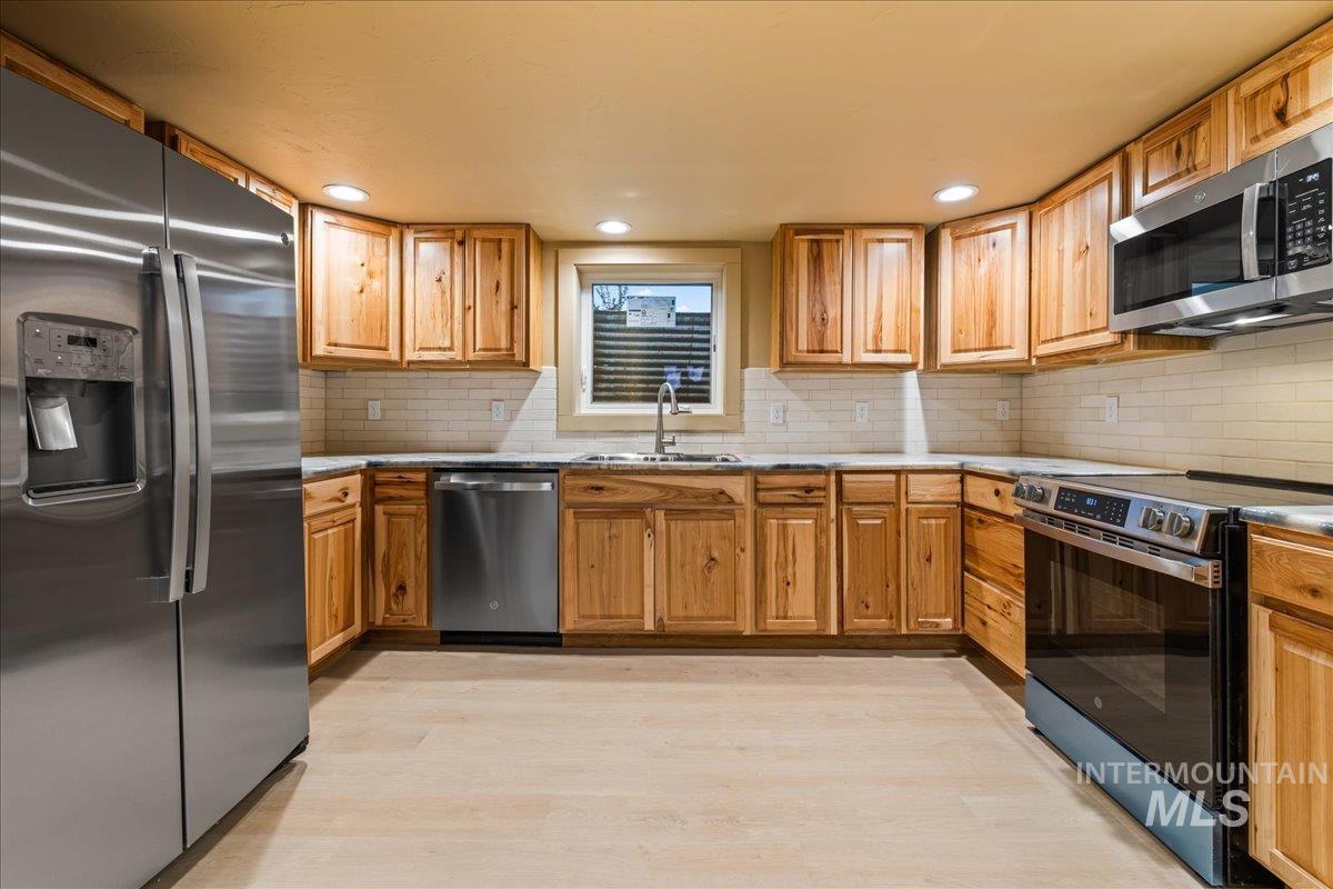 Kitchen with stainless steel appliances, light stone counters, tasteful backsplash, light wood-style floors, and recessed lighting