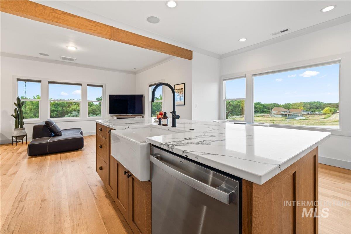 Kitchen with brown cabinets, an island with sink, stainless steel dishwasher, open floor plan, and beam ceiling