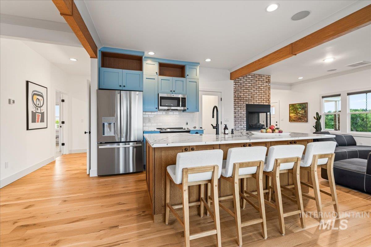 Kitchen featuring beamed ceiling, open floor plan, blue cabinetry, appliances with stainless steel finishes, and tasteful backsplash