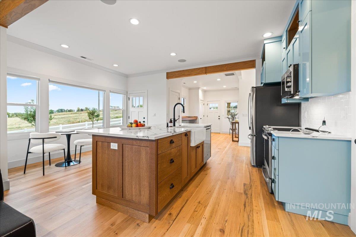 Kitchen with a kitchen island with sink, blue cabinetry, light stone counters, tasteful backsplash, and light wood-style floors