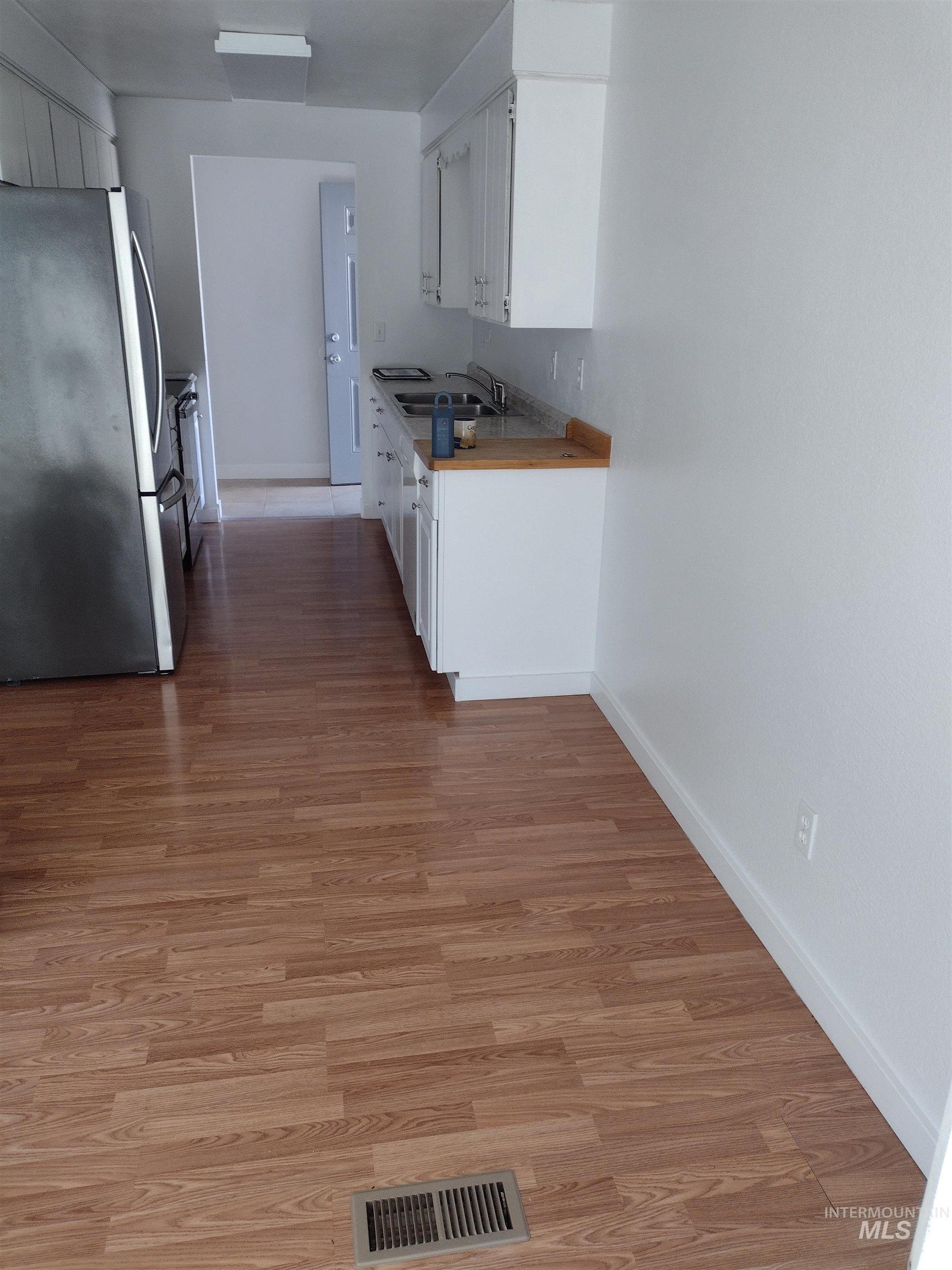 Kitchen featuring freestanding refrigerator, white cabinets, light wood-style flooring, and light countertops