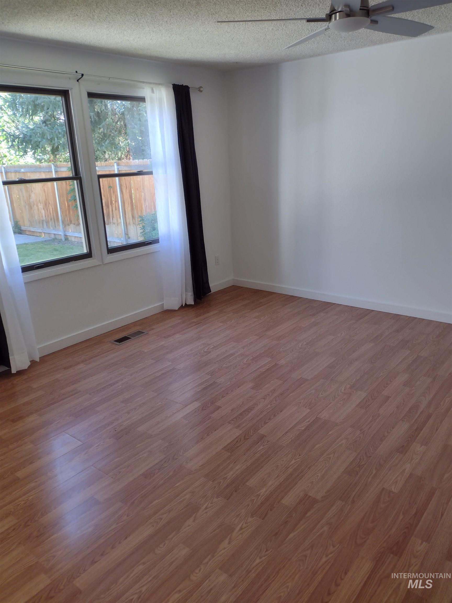 Empty room featuring light wood-style flooring, a textured ceiling, and a ceiling fan