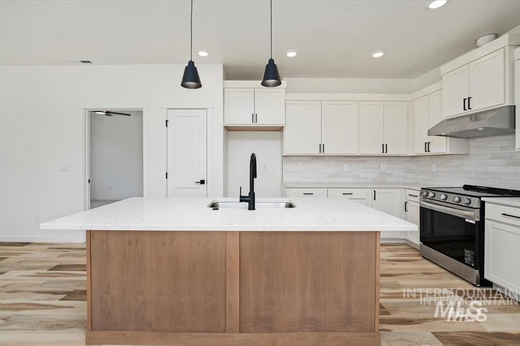 Kitchen featuring stainless steel electric stove, light stone countertops, backsplash, decorative light fixtures, and under cabinet range hood