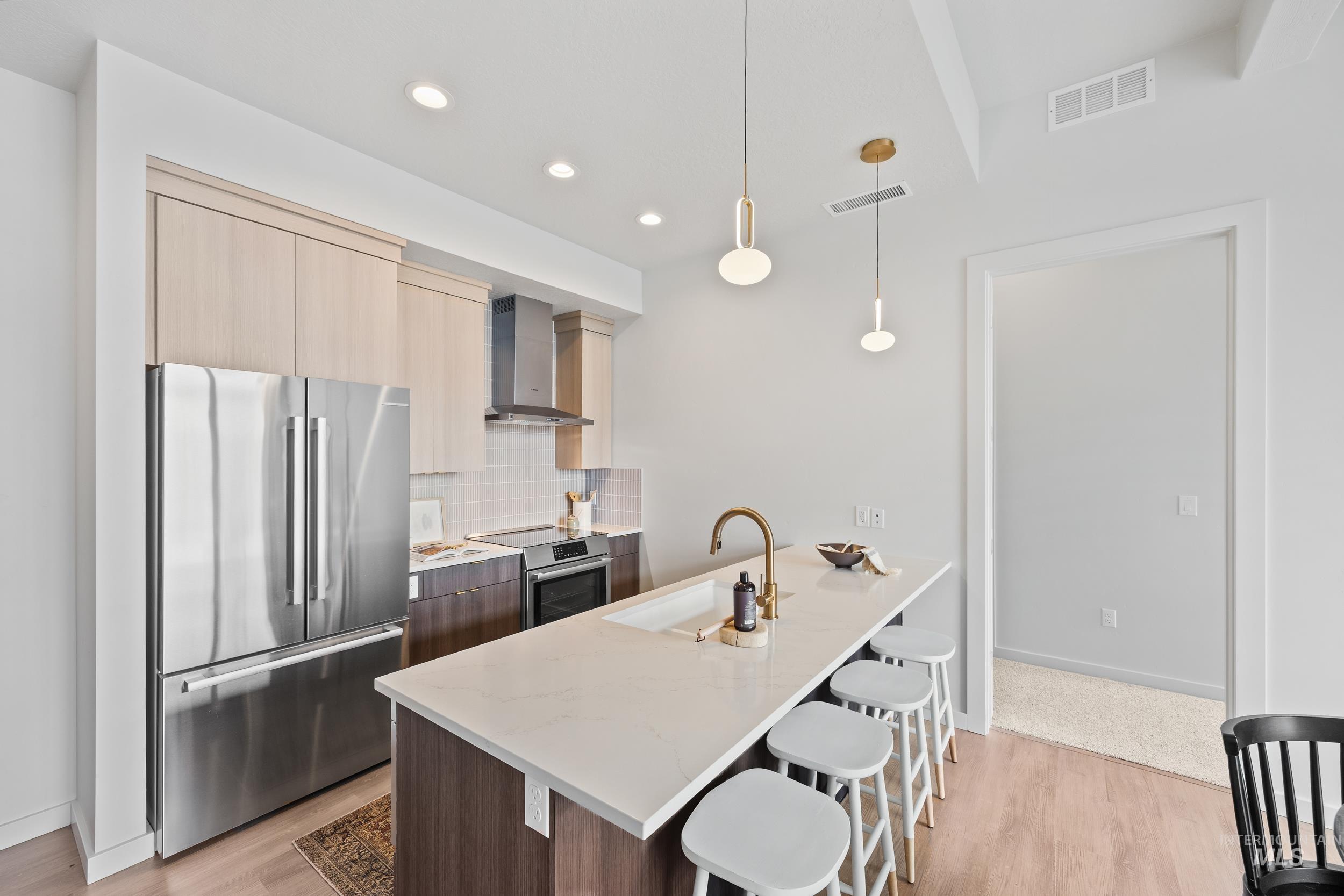 Kitchen featuring modern cabinets, appliances with stainless steel finishes, light stone counters, decorative backsplash, and a kitchen bar