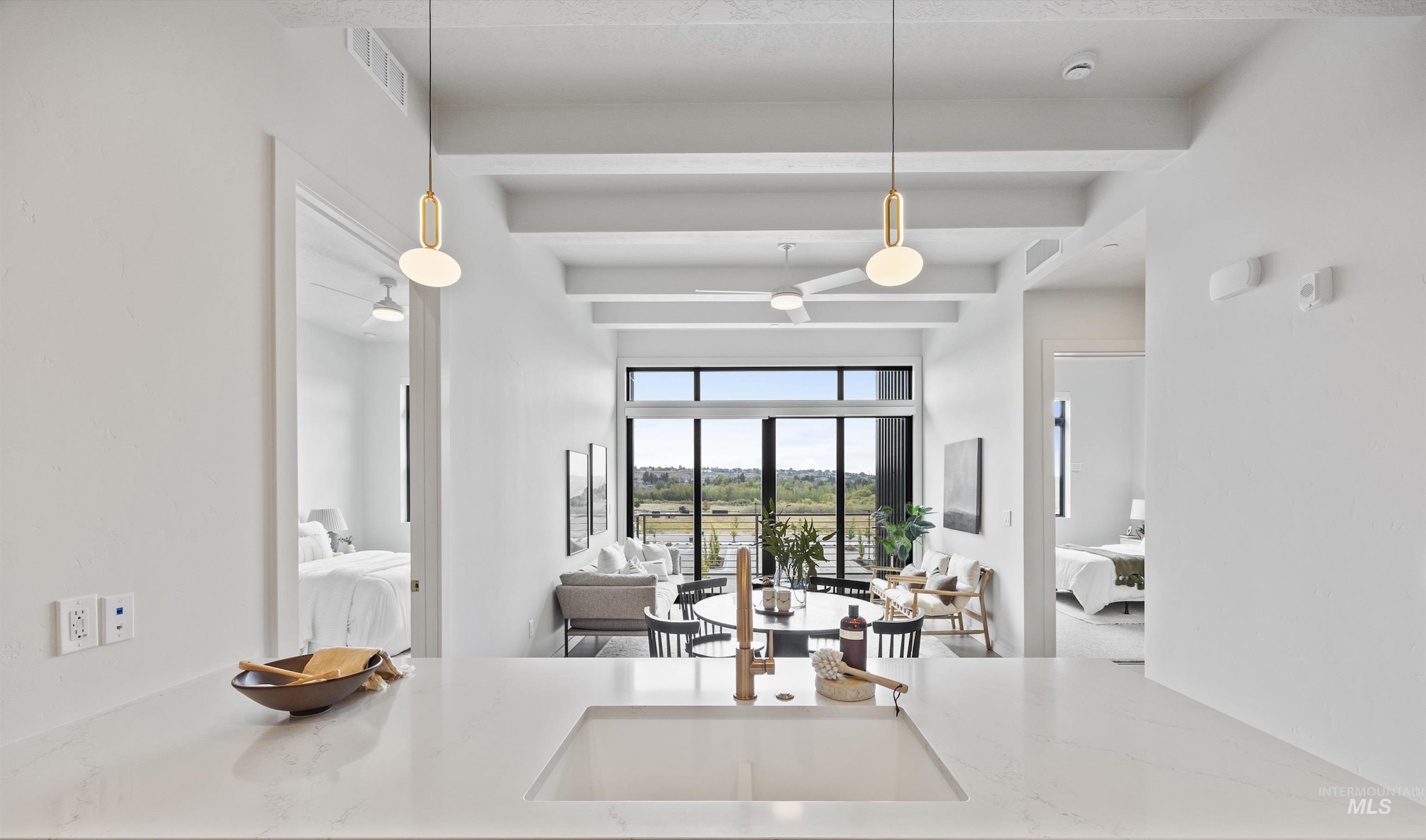 Kitchen with light stone countertops, pendant lighting, beamed ceiling, and open floor plan