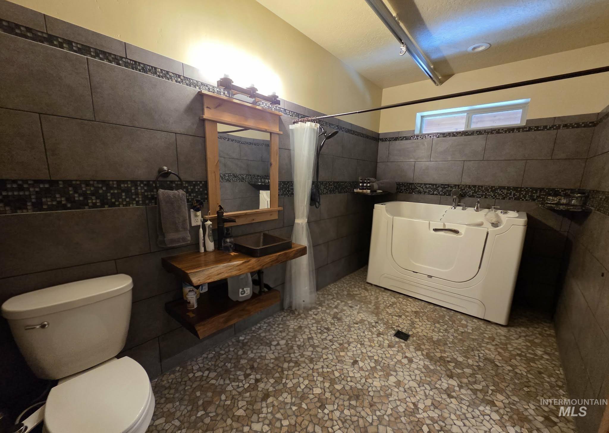 Full bath with tile walls, washer / dryer, a tub, and a shower with shower curtain