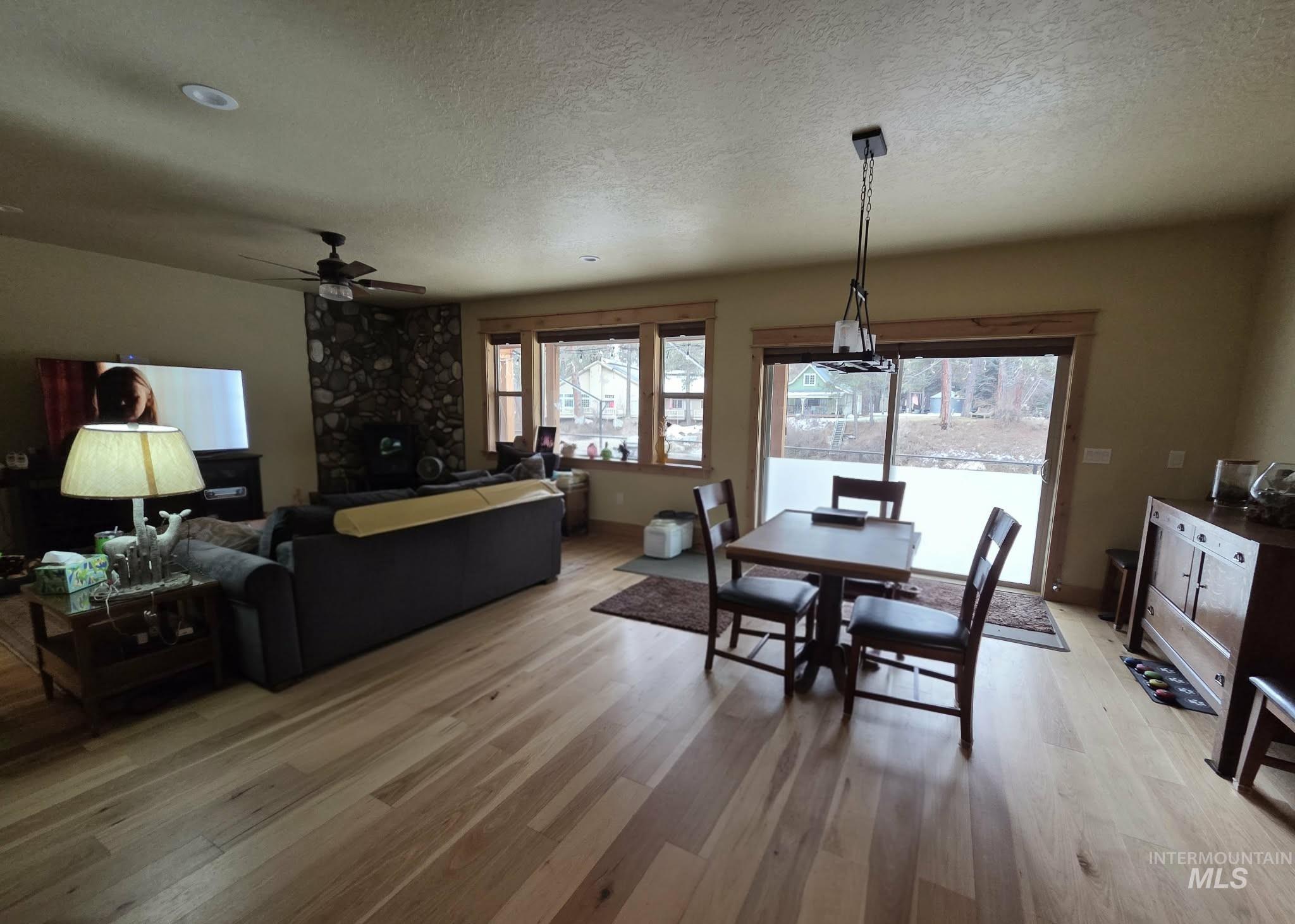 Dining room with light wood-type flooring, a textured ceiling, a ceiling fan, and a fireplace