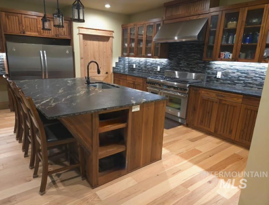 Kitchen featuring stainless steel appliances, range hood, wood finish cabinetry, and glass insert cabinets