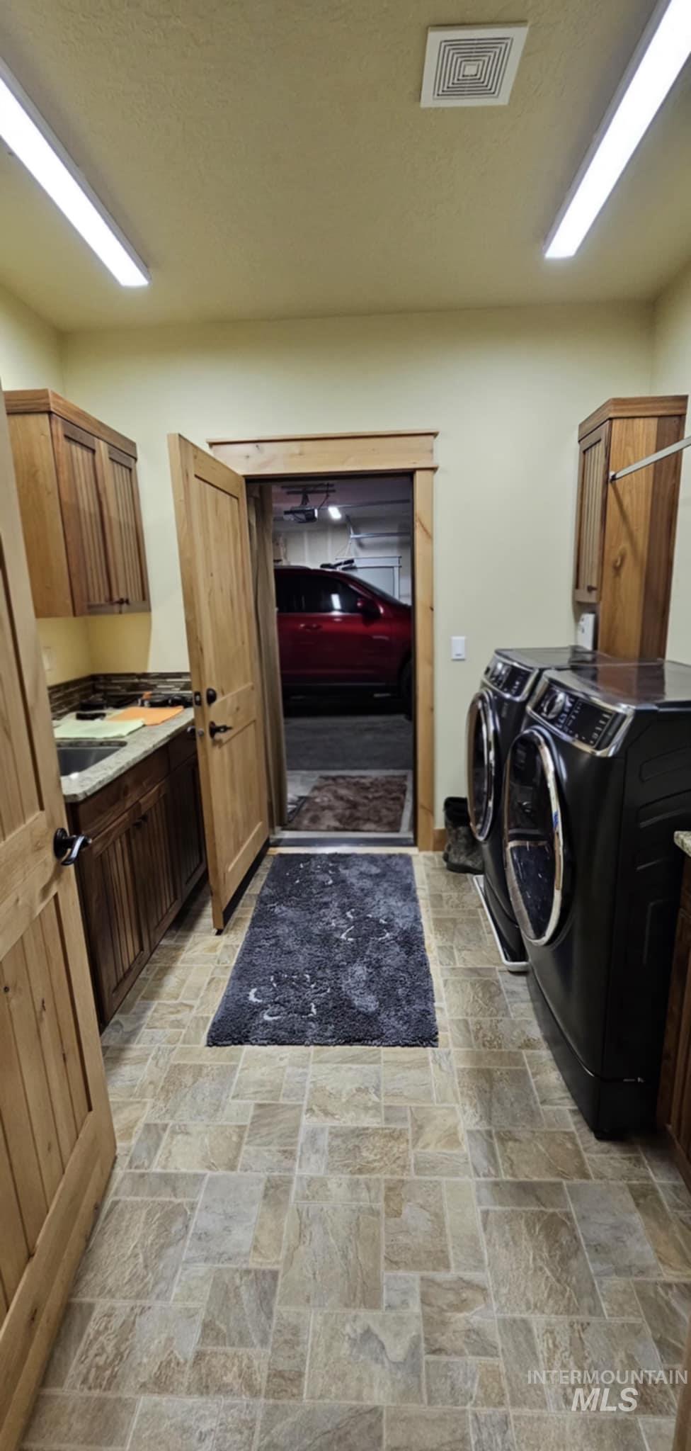 Laundry area featuring stone finish flooring, cabinet space, and washing machine and dryer