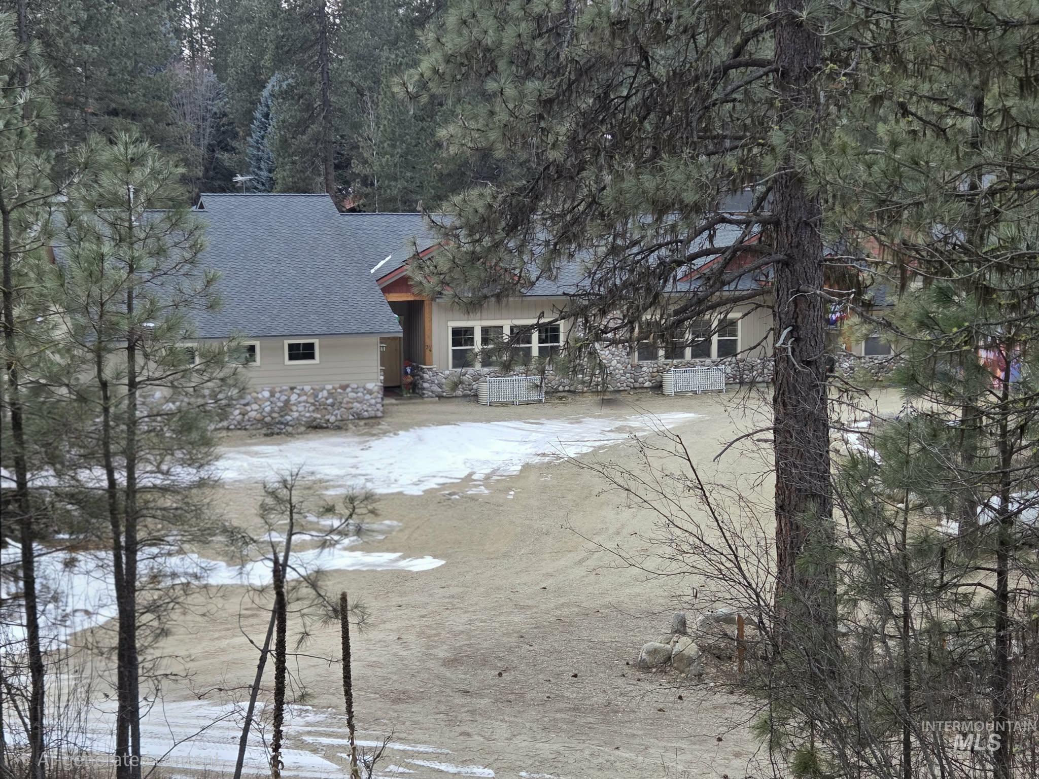 Snow covered property featuring roof with shingles and stone siding