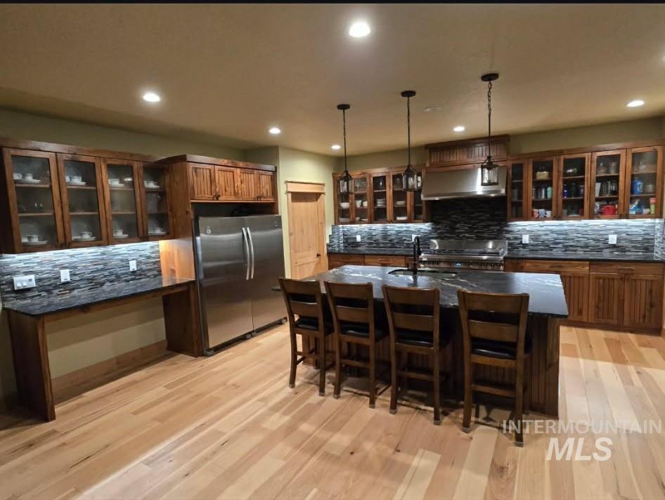Kitchen with glass fronted cabinets, stainless steel appliances, pendant lighting, and light wood finished floors