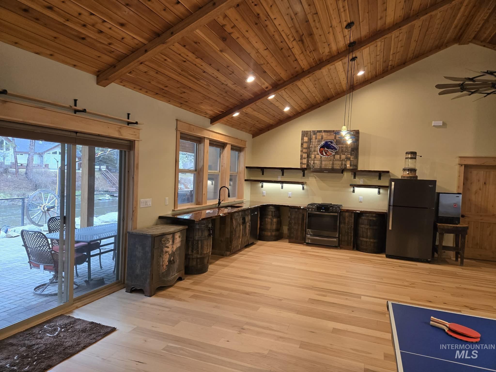 Kitchen featuring a high wooden beamed ceiling, stainless steel range with gas stovetop, light wood-style floors, freestanding refrigerator, and decorative light fixtures