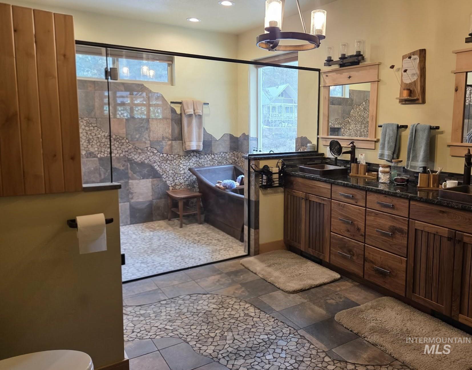 Bathroom featuring tiled shower, double vanity, healthy amount of natural light, stone tile floors, and recessed lighting
