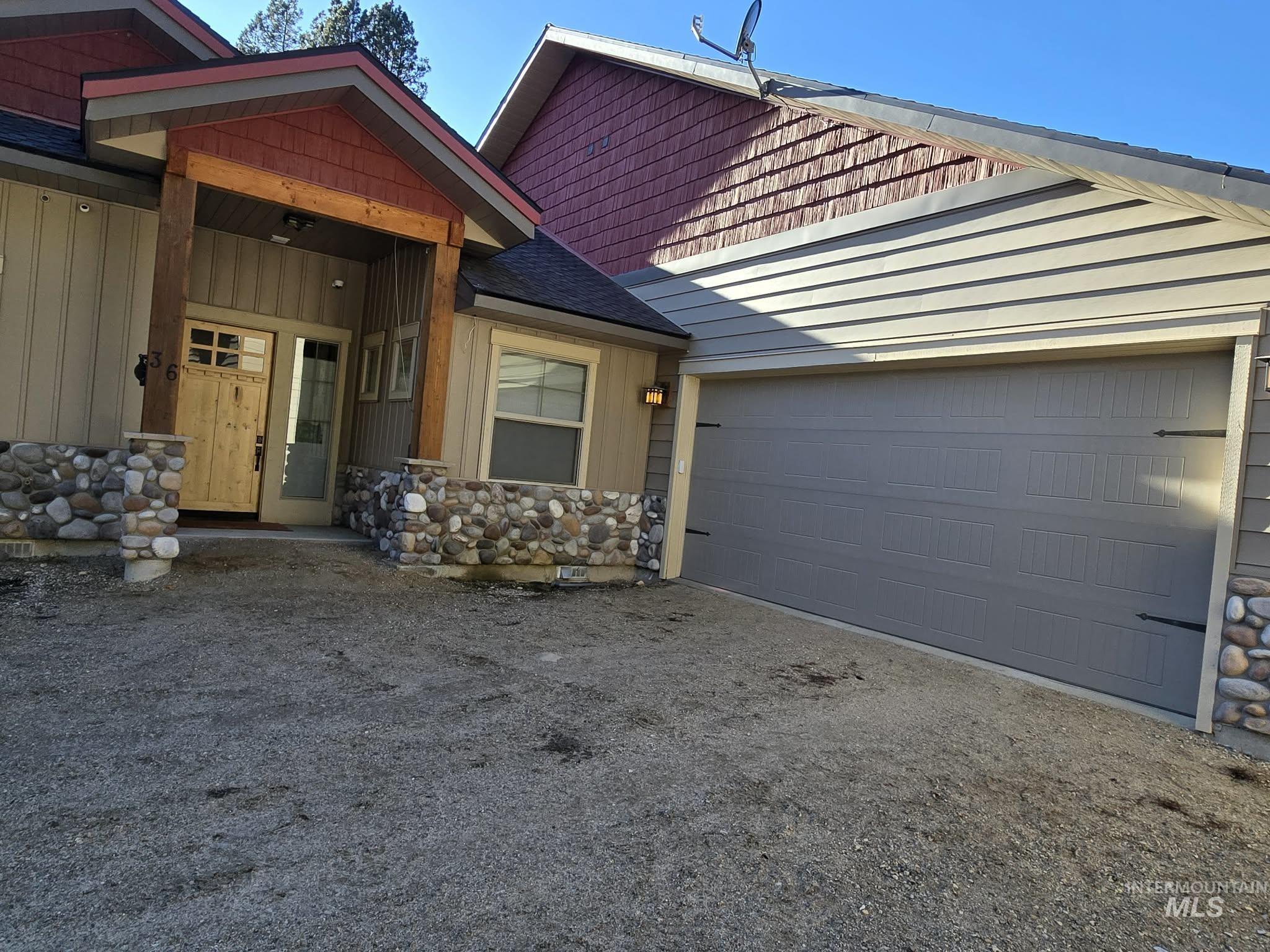 View of front of home featuring an attached garage, stone siding, a porch, driveway, and roof with shingles