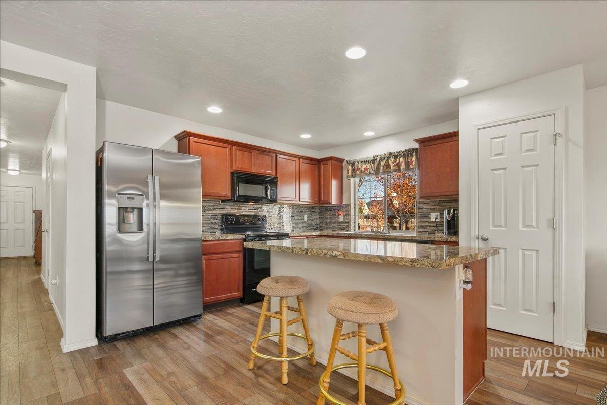 Kitchen with black appliances, light stone counters, decorative backsplash, a breakfast bar area, and light wood finished floors