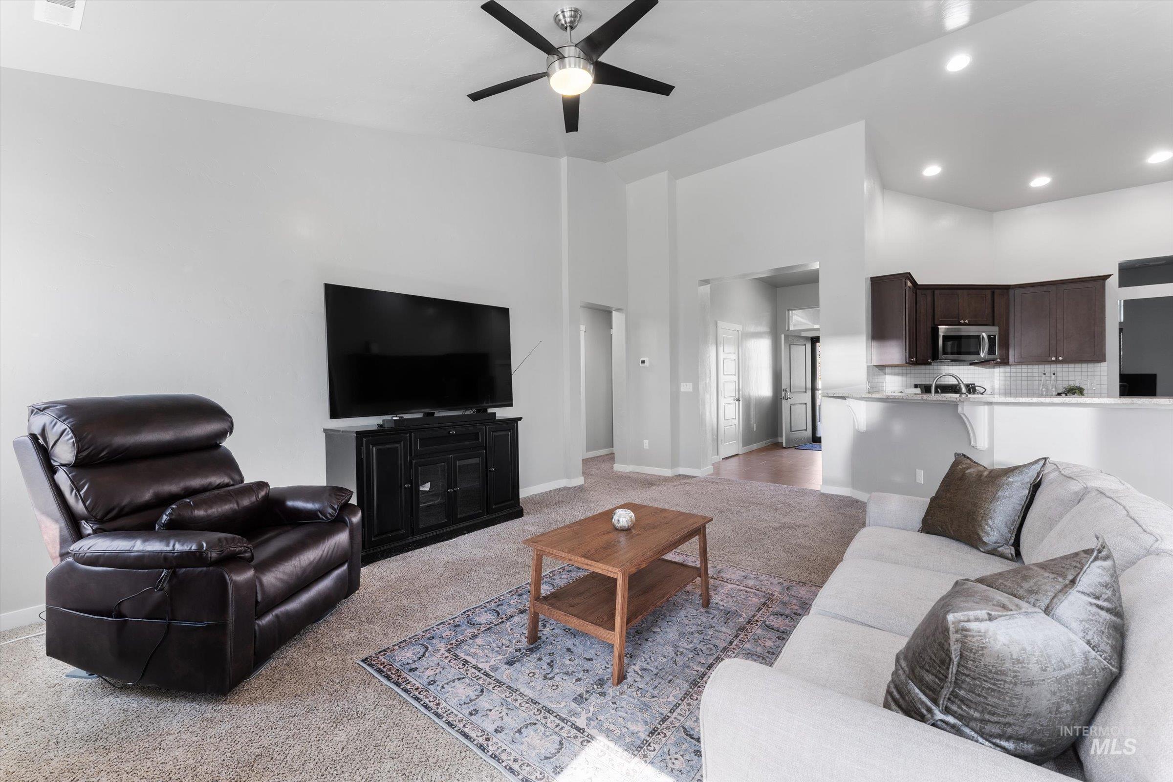 Living area with light carpet, ceiling fan, a high ceiling, and recessed lighting