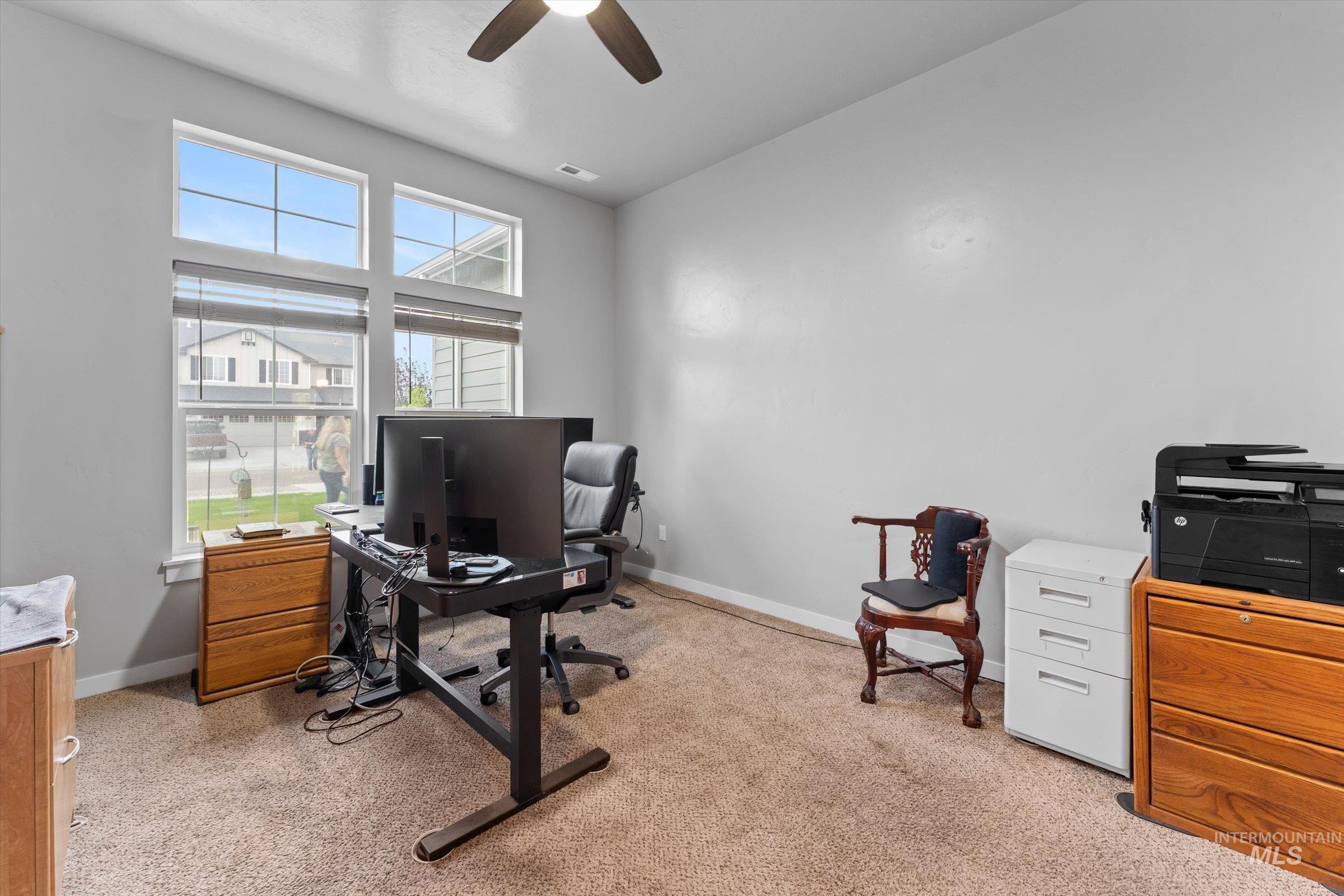 Home office with light carpet and a ceiling fan