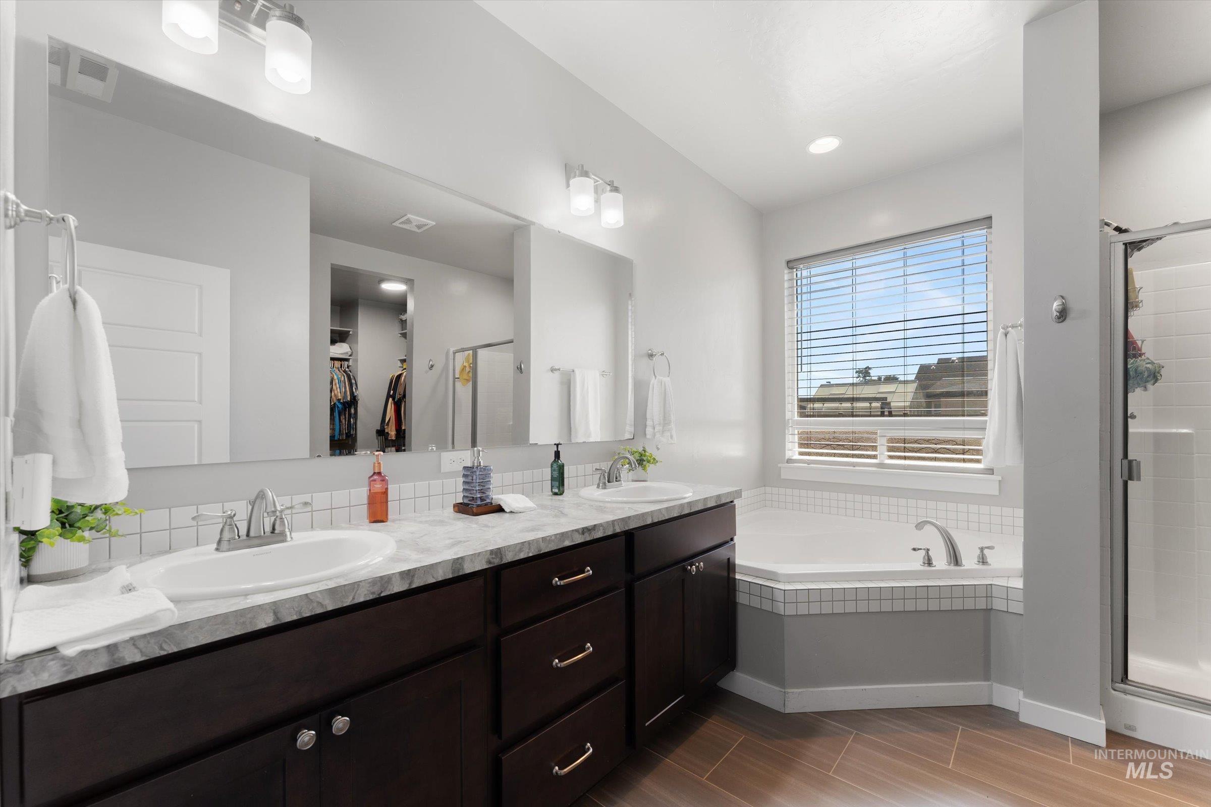 Full bath featuring a garden tub, a stall shower, a walk in closet, double vanity, and wood finish floors