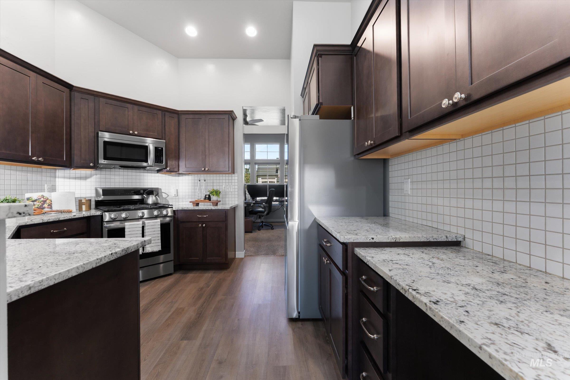Kitchen featuring stainless steel appliances, light stone counters, dark wood-style flooring, and dark brown cabinets