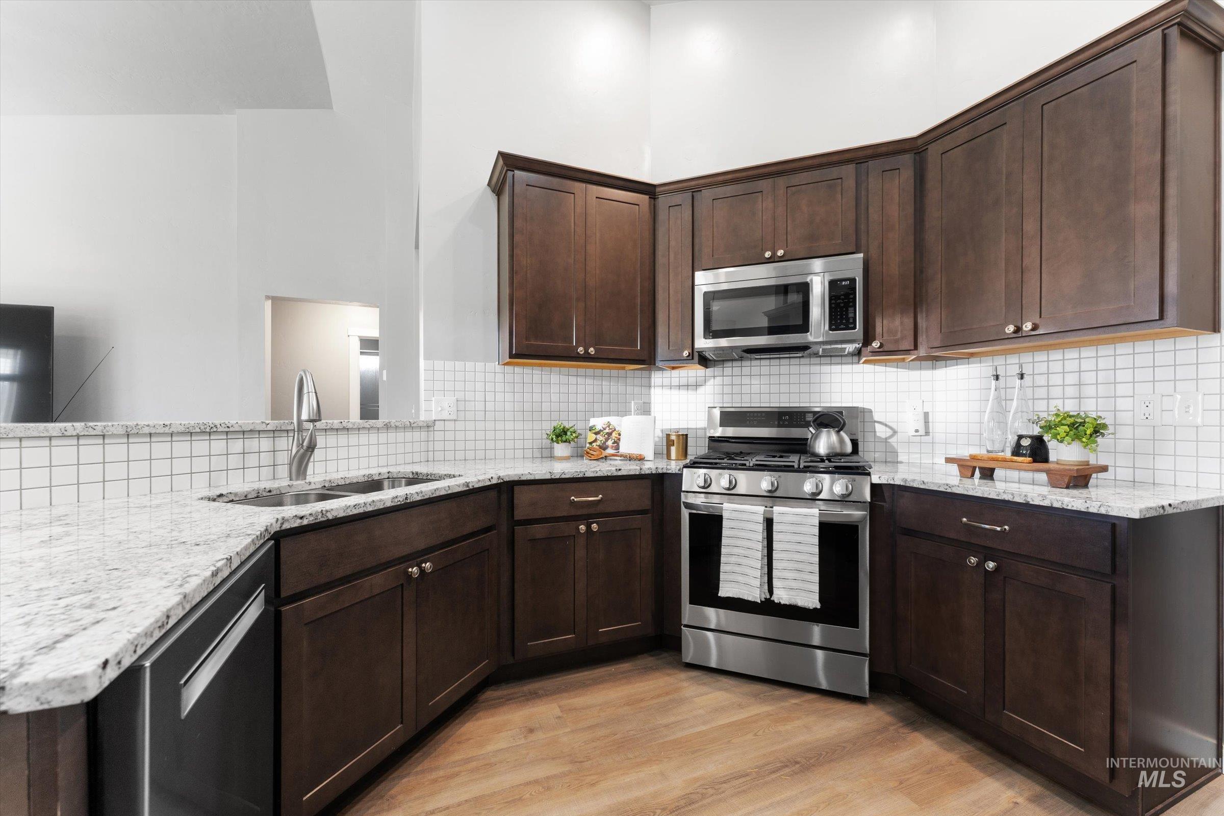 Kitchen featuring stainless steel appliances, light stone counters, dark brown cabinets, light wood-style flooring, and a high ceiling