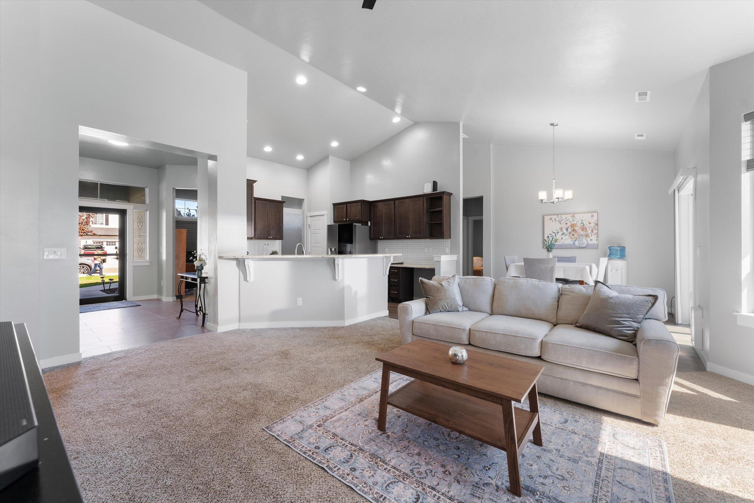 Living area featuring light carpet, high vaulted ceiling, a chandelier, and recessed lighting