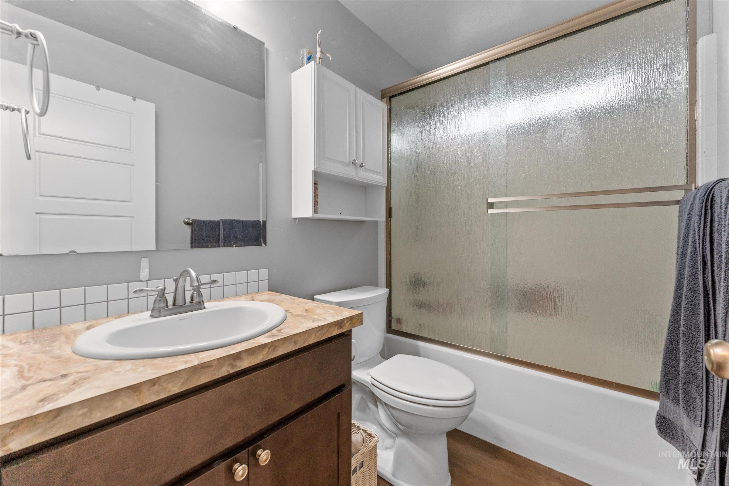 Full bath featuring bath / shower combo with glass door, vanity, and wood finished floors